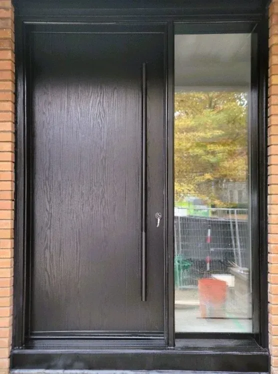 Modern black entry door with full-height glass sidelight on a brick Bradford home